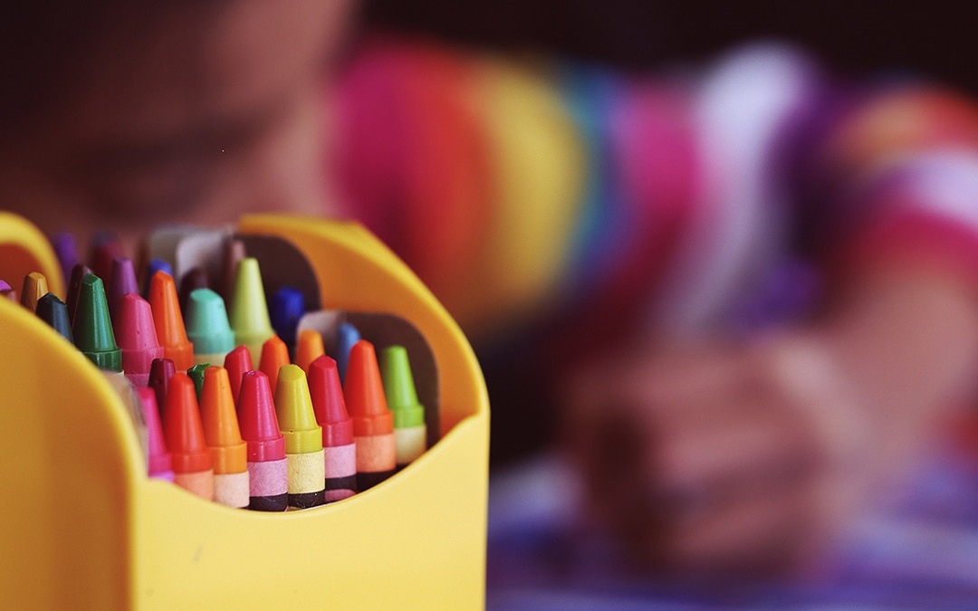 Box of crayons with child coloring in back ground - by Aaron Burden (via Unsplash)